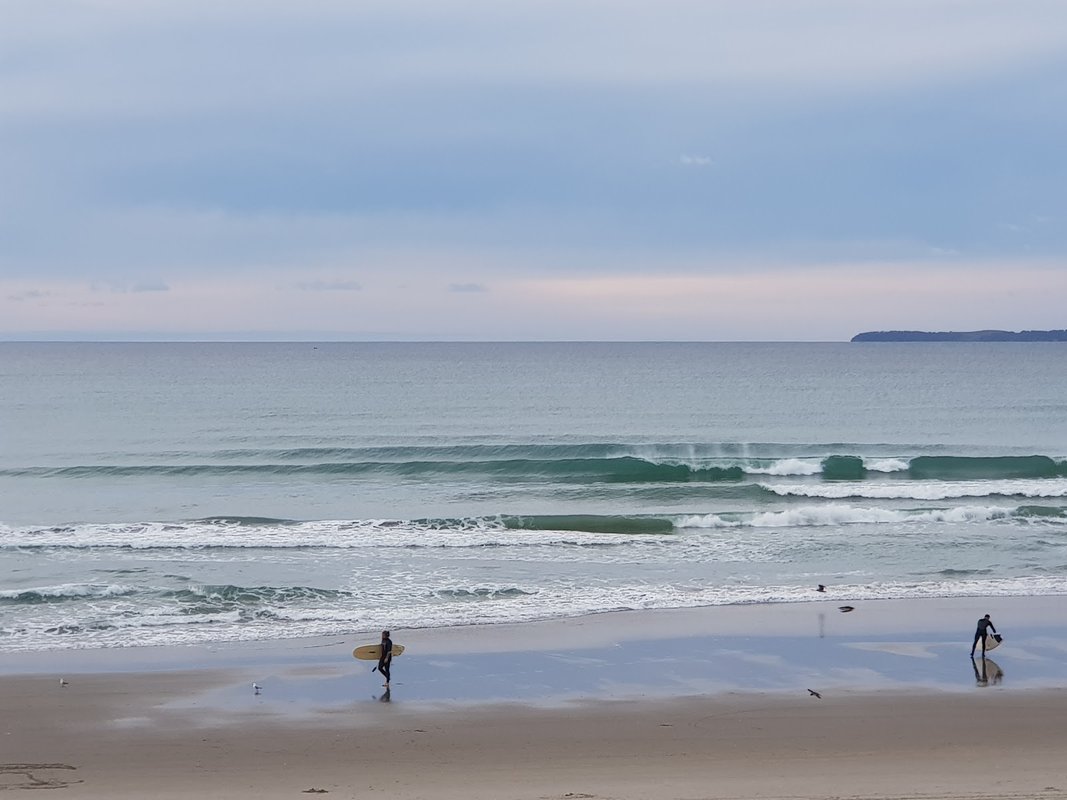 Surfers walking out at dawn, a faint headland on the horizon, Matarangi surf spot, Coromandel, New Zealand.