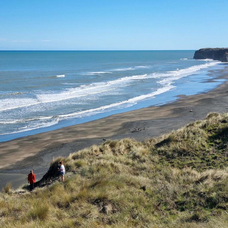 Black-sand beach curving to the cliffs at Pātea on a clean day, Pātea surf spot, Taranaki / SH45, New Zealand.